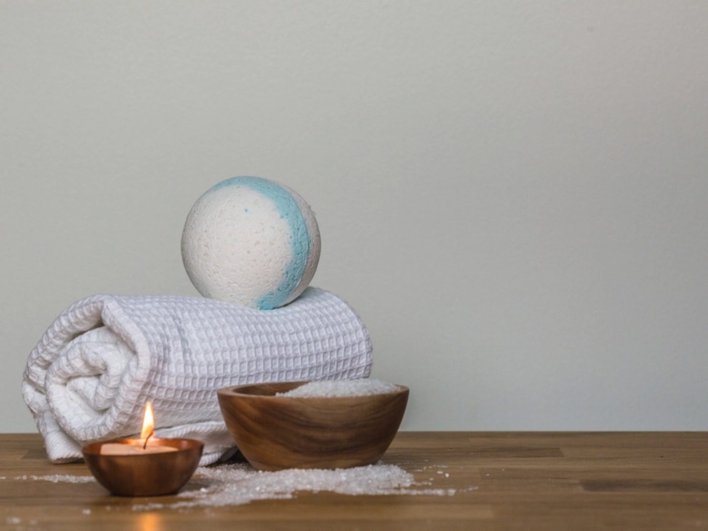 A folded towel, wooden bowl and candle on a tray