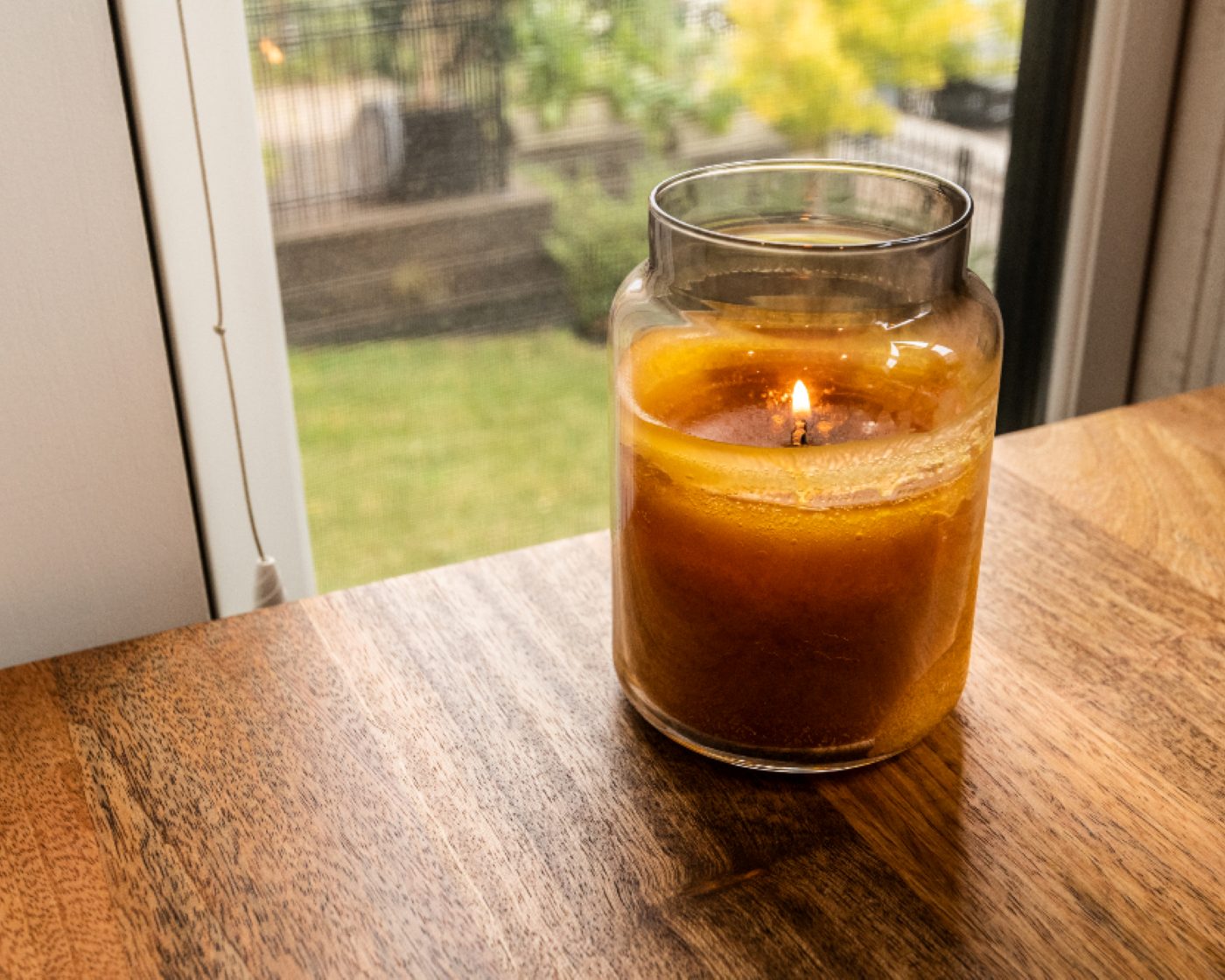 An amber jar candle burning on a table by a window