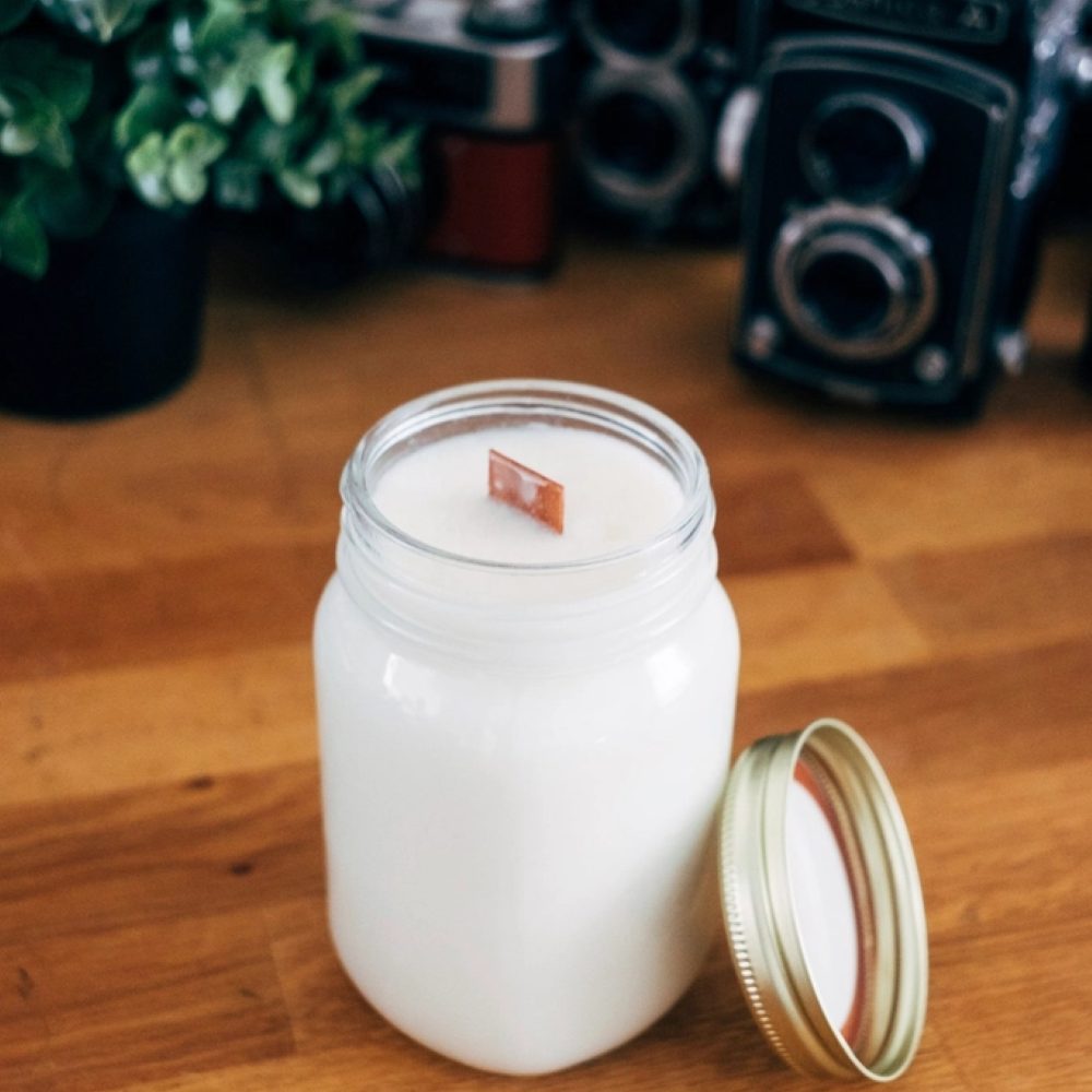 A white candle in a glass jar with its lid beside it
