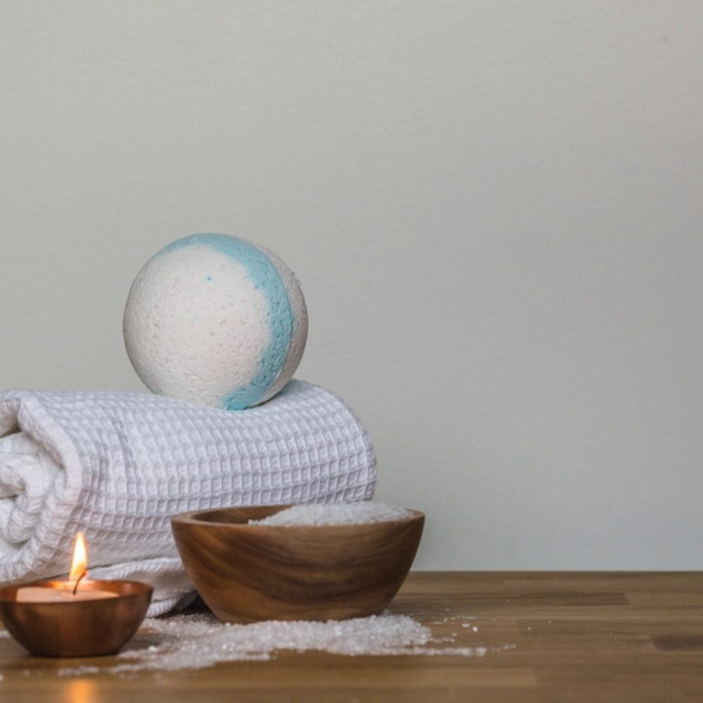 A folded towel, wooden bowl and candle on a tray
