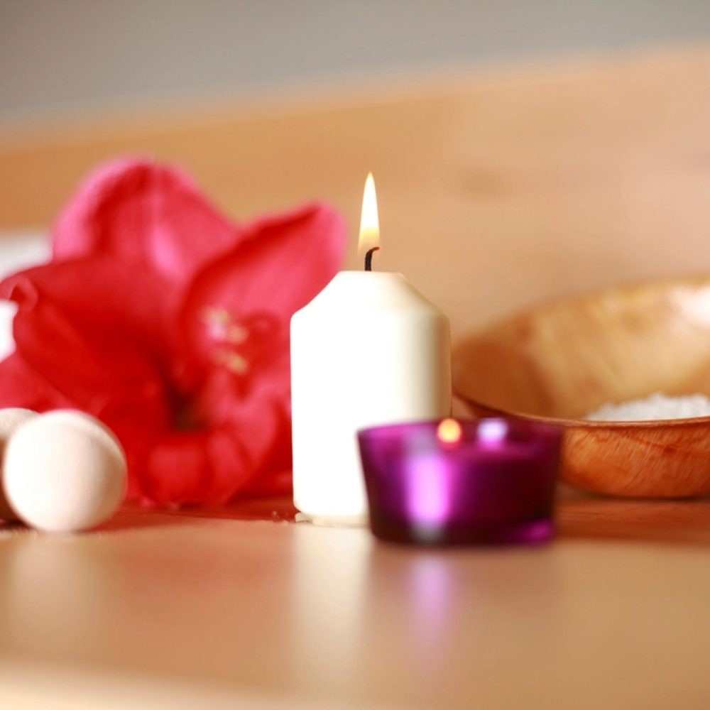 Candles arranged with a red bloom and a wooden bowl