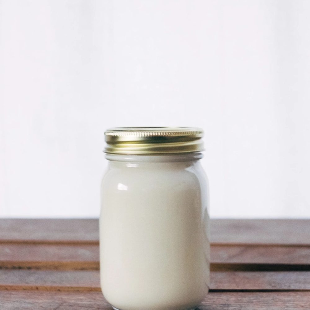 A white candle in a glass jar on a wooden surface